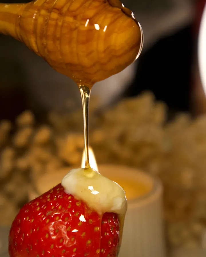 Honey dripping over a strawberry dipped in mishti doi