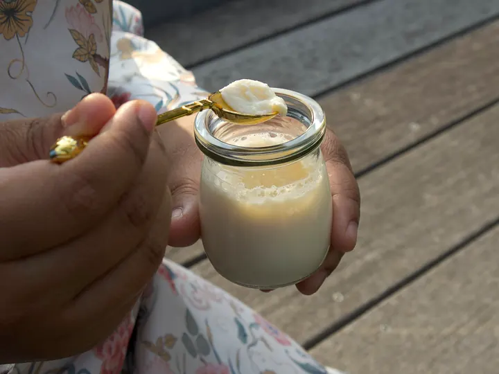 A hand holding a jar of mishti doi with a gold spoon