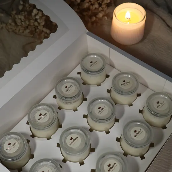 Twelve jars of Doilicious mishti doi in a white box beside a lit candle